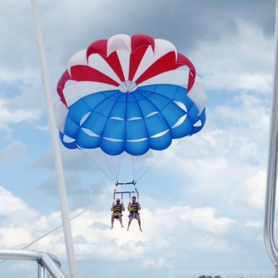 Two people flying under a red, white, and blue parasail