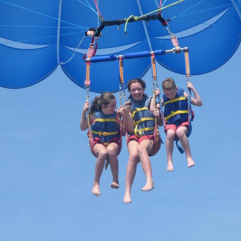 Three kids smiling as they fly under the prasail