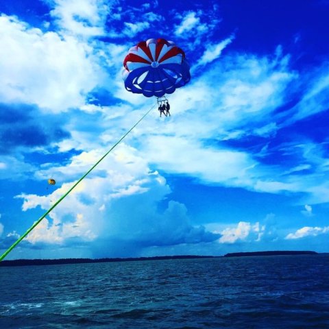 A red, white, and blue parasail in a cloudy blue sky