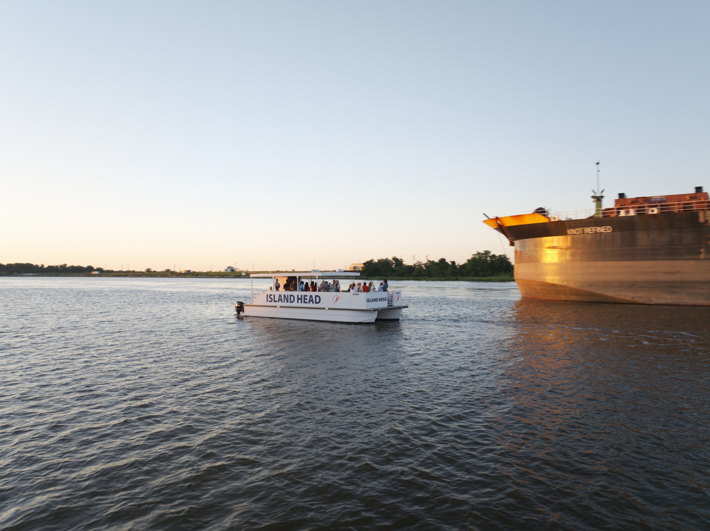Small tour boat near a large cargo ship on a calm river at sunset.